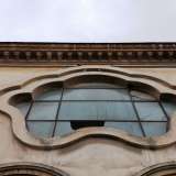 Ancora pi� in alto si fa notare un�apertura a vetri polilobata iscritta in una cornice in pietra. Chiude il prospetto un cornicione dentellato e un parapetto con elementi geometrici che corre lungo tutto il perimetro delimitando il terrazzo